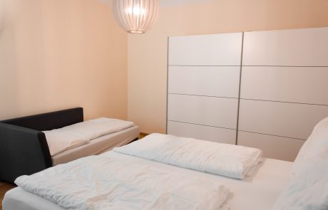 IMG_2332 Doppelbett mit weißer Bettwäsche und Einzelbett in schlicht eingerichtetem Schlafzimmer mit großem weißen Kleiderschrank und runder Deckenleuchte